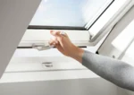 Mână deschizând fereastra VELUX GLU 0061B cu mâner jos, ideală pentru încăperi umede