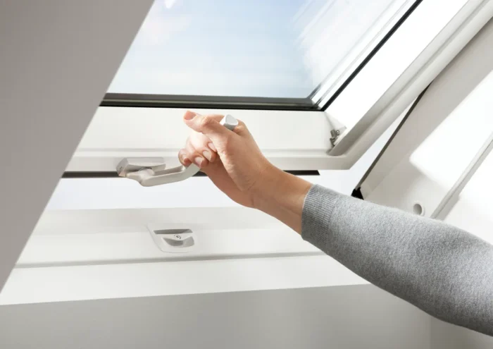 Mână deschizând fereastra VELUX GLU 0061B cu mâner jos, ideală pentru încăperi umede