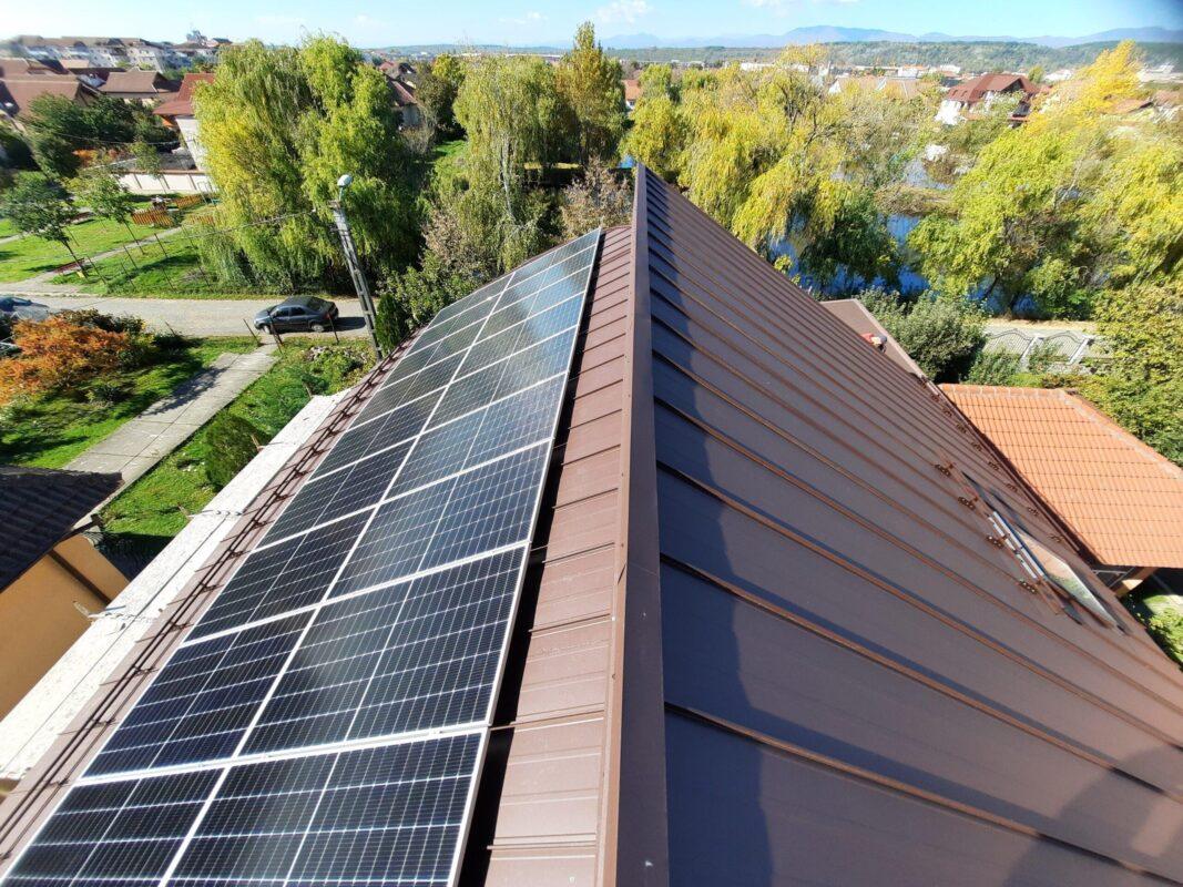 Coama acoperișului și învelitoarea din tablă, lângă un versant cu panouri fotovoltaice