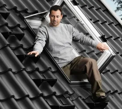 Bărbat ieșind prin fereastra de acces VELUX GXU cu finisaj alb, montată pe acoperiș din țiglă