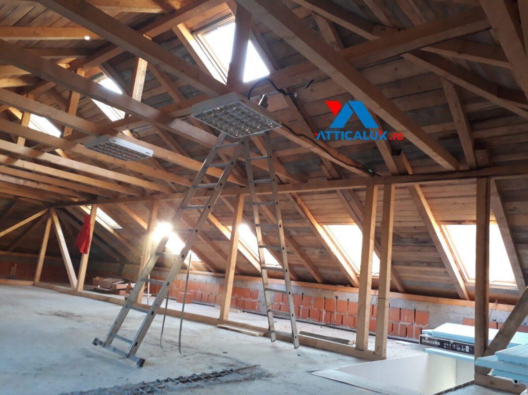 Mansardă în lucru, cu structură din lemn și ferestre care aduc lumină în interior